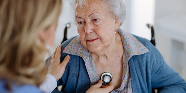 Elderly woman in wheelchair with caregiver using stethoscope